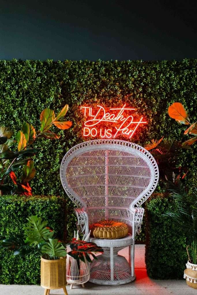 White peacock chair in front of greenery wall with Led light sign
